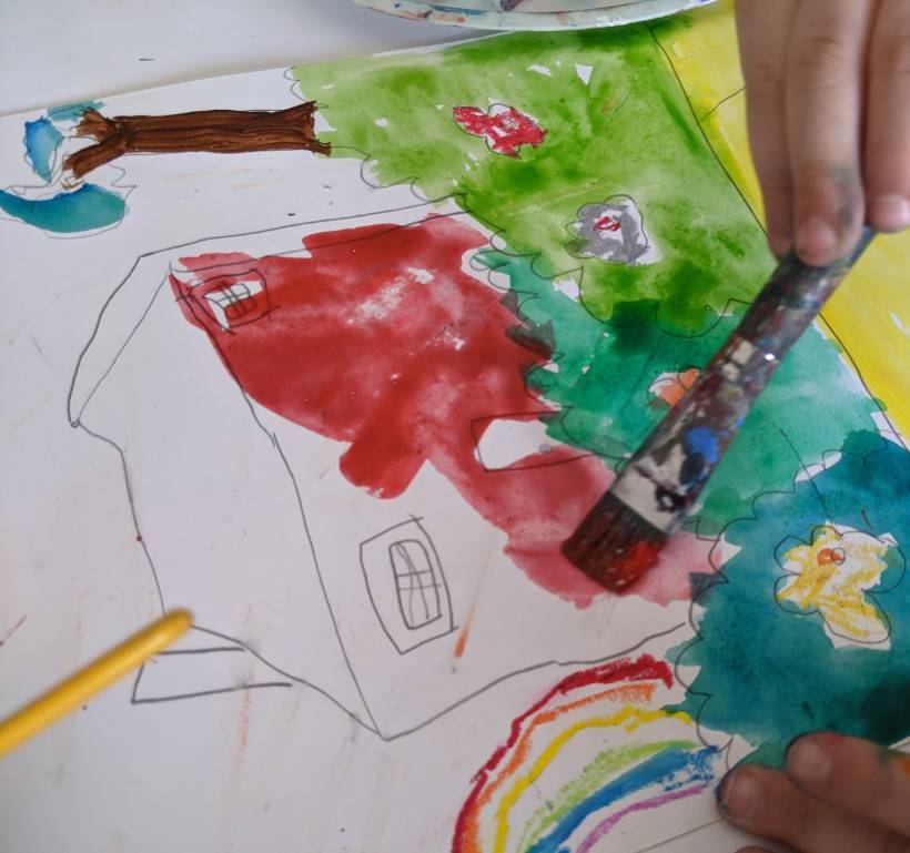 A child painting a watercolour house, tree and rainbow