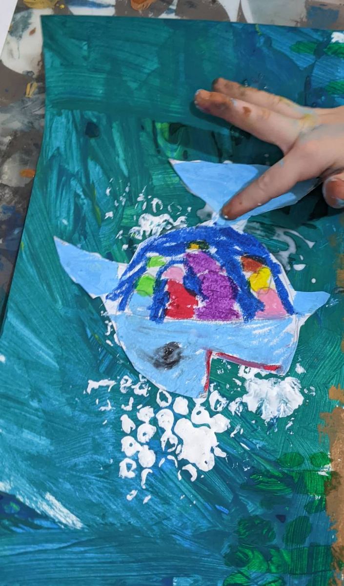 A child making a bright paper-collage rainbow fish