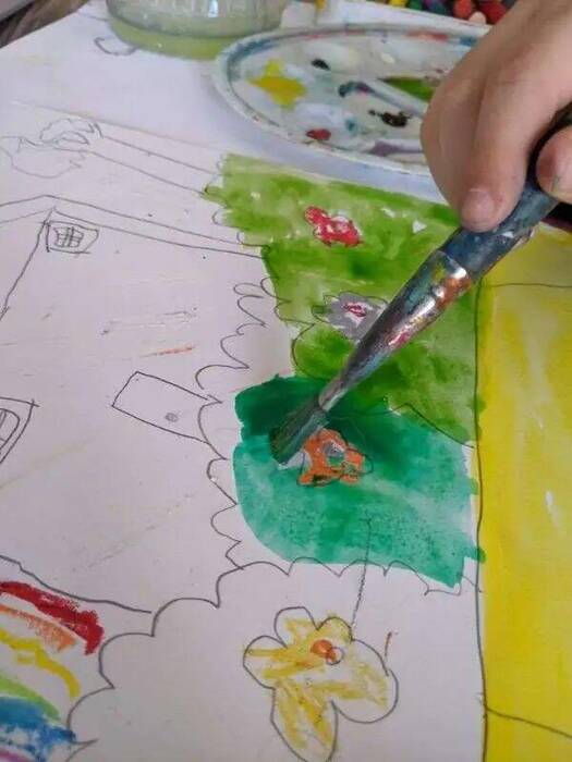A child watercolour-painting a house scene