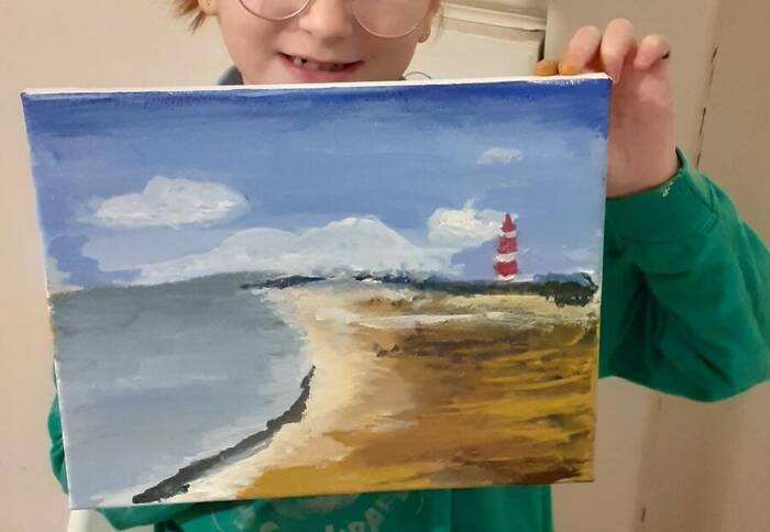 A child holding up a lighthouse beach painting