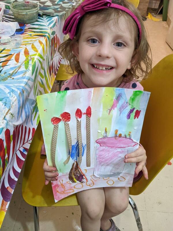 A young Littlies student holding up her painting